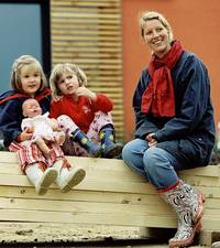 Mutter mit Kindern vor einem Holzhaus